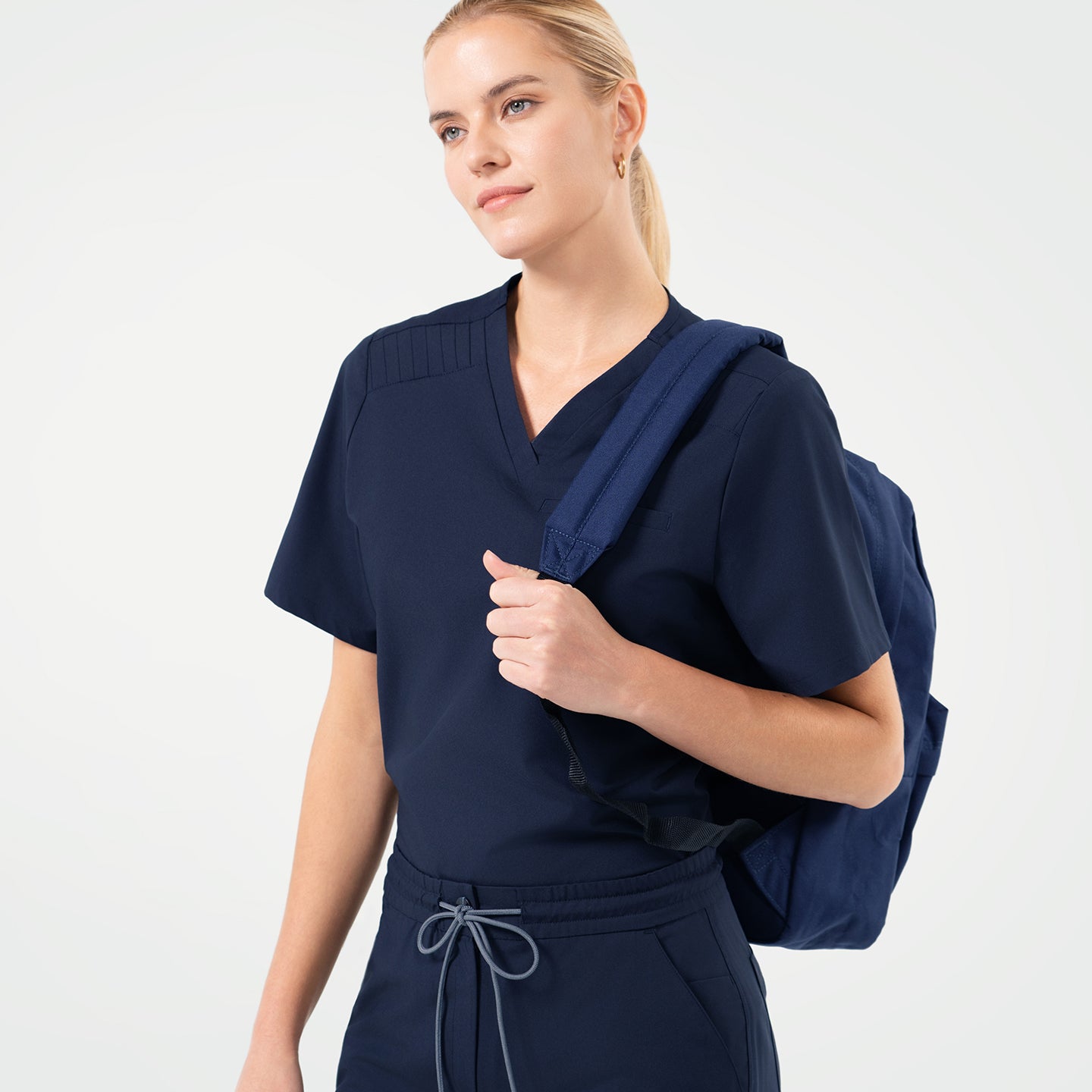 Image of Eco Navy scrub top with chest pocket, paired with matching scrub pants, styled with a navy backpack for a modern professional look.